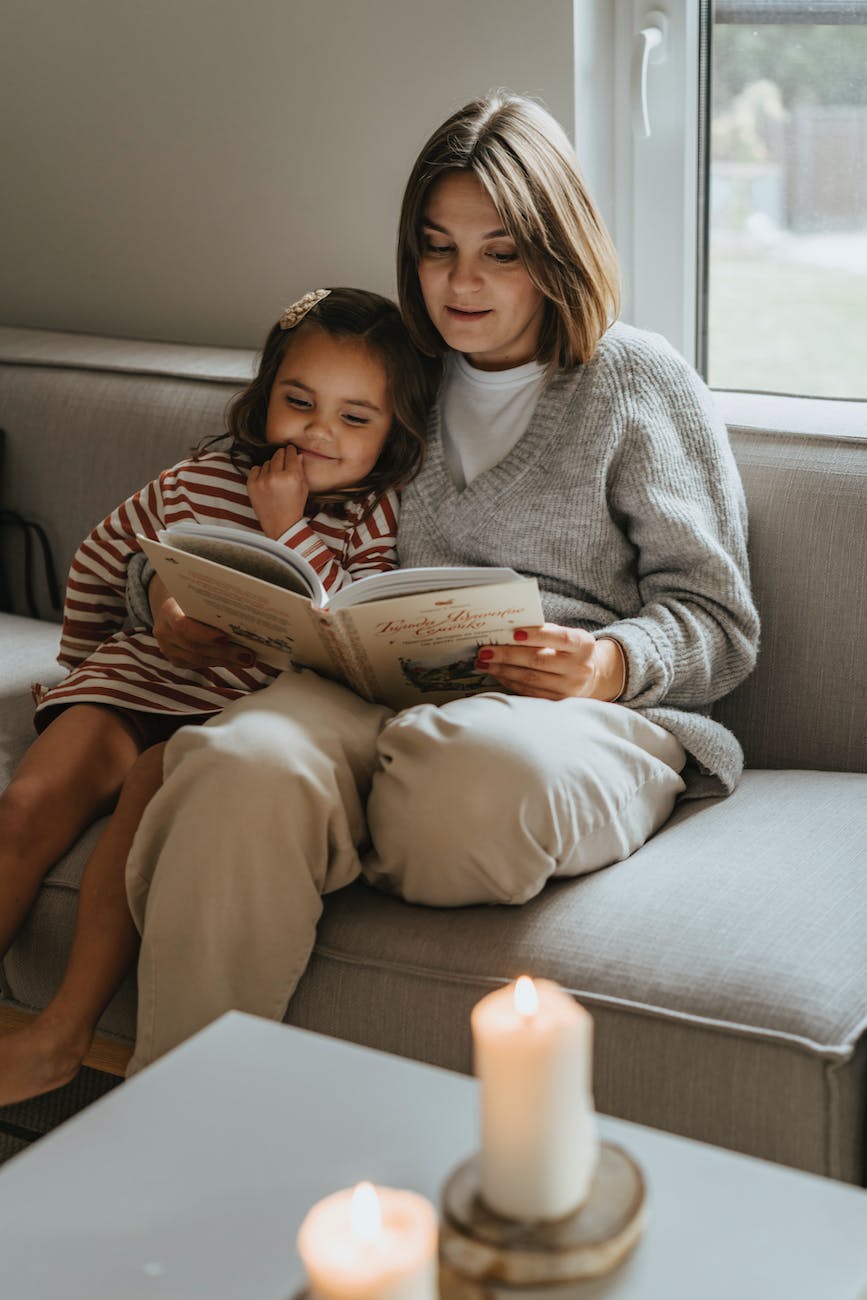 a mother and daughter reading a book on a couch