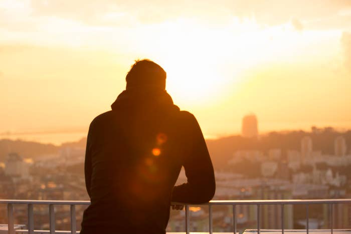 Person in a hoodie overlooks a cityscape at sunrise from a balcony