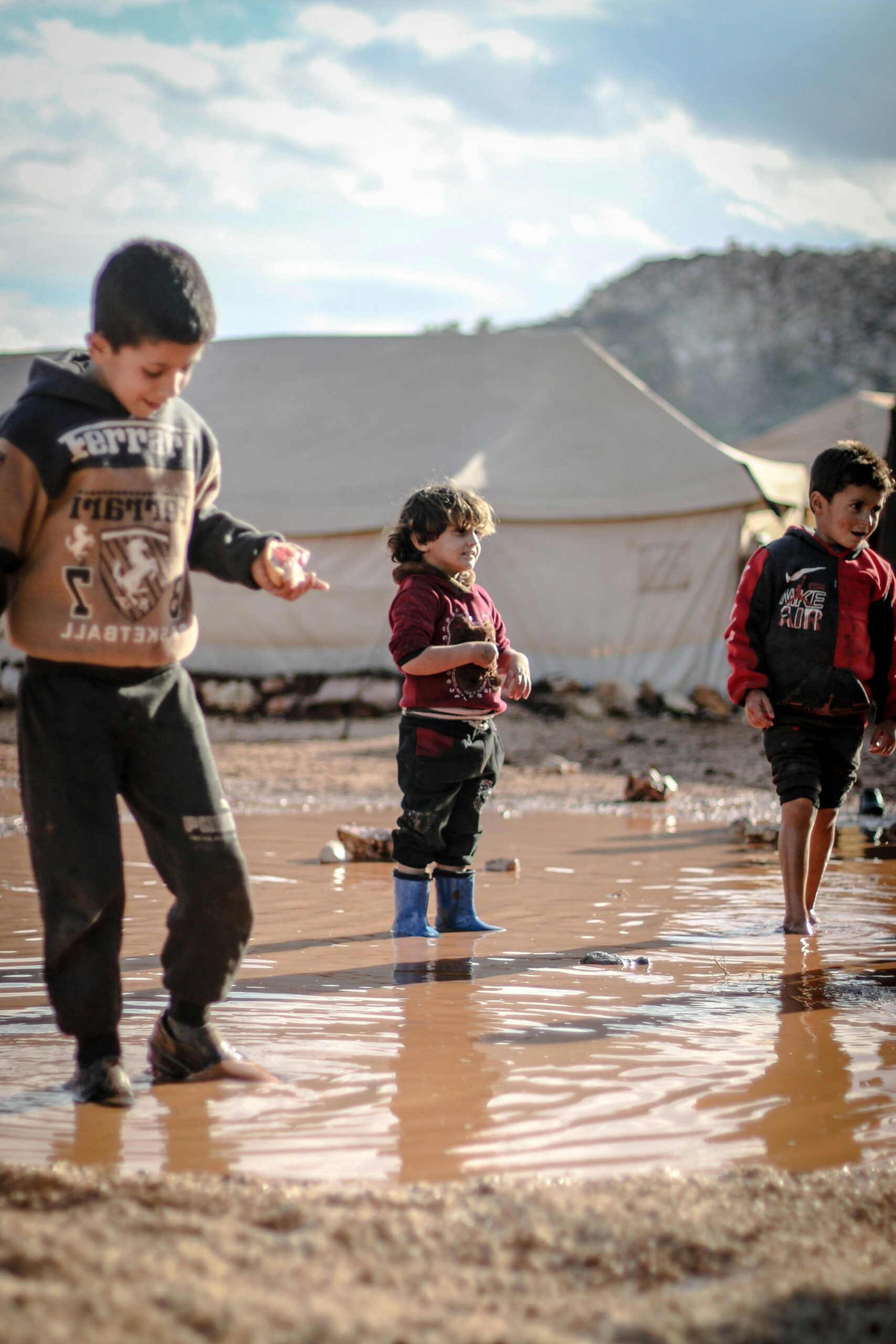 Refugee Children enjoying playtime in a muddy puddle at a refugee camp in Idlib, Syria.