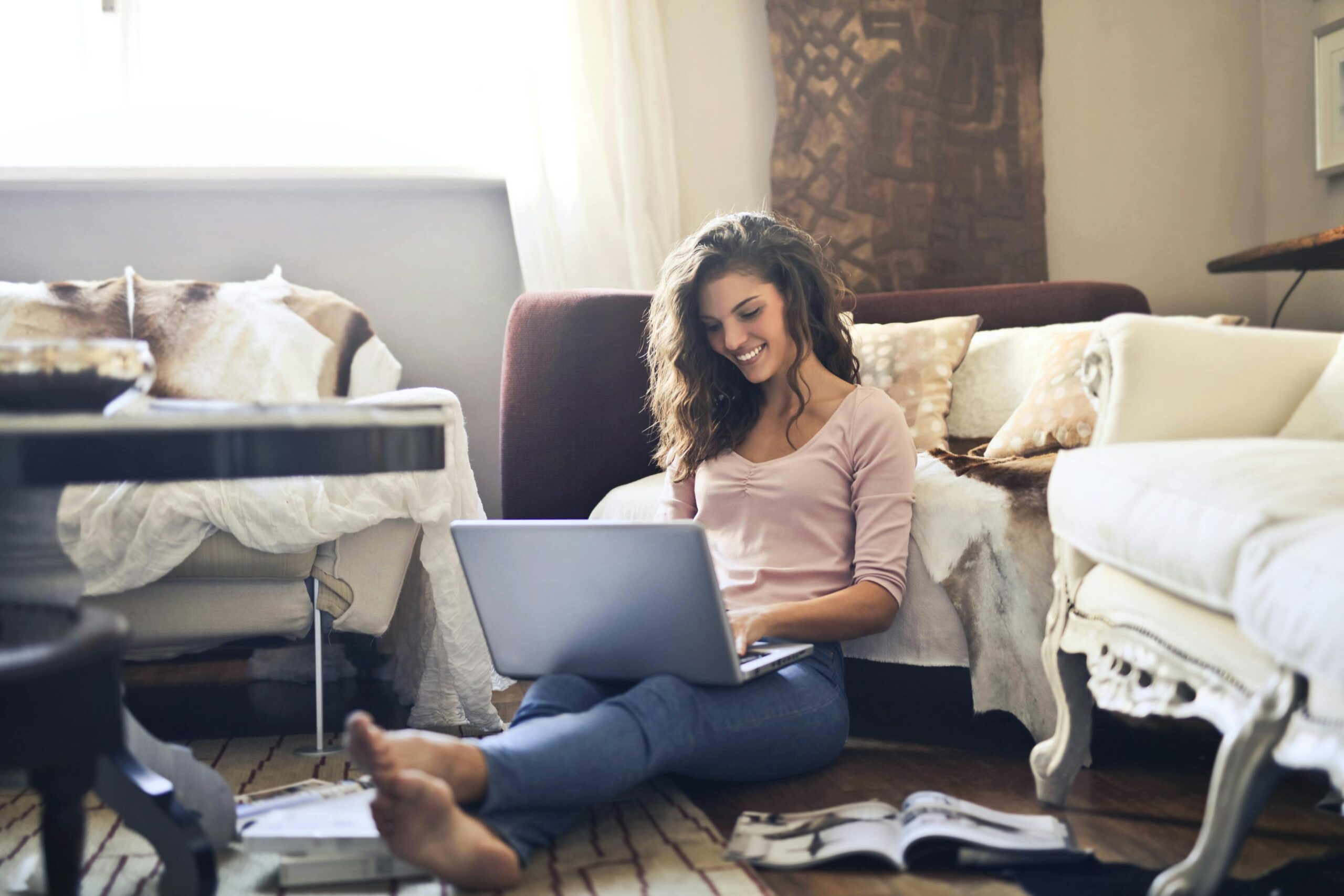 Smiling woman using a laptop seated on the floor in a cozy living room, working remotely work from home