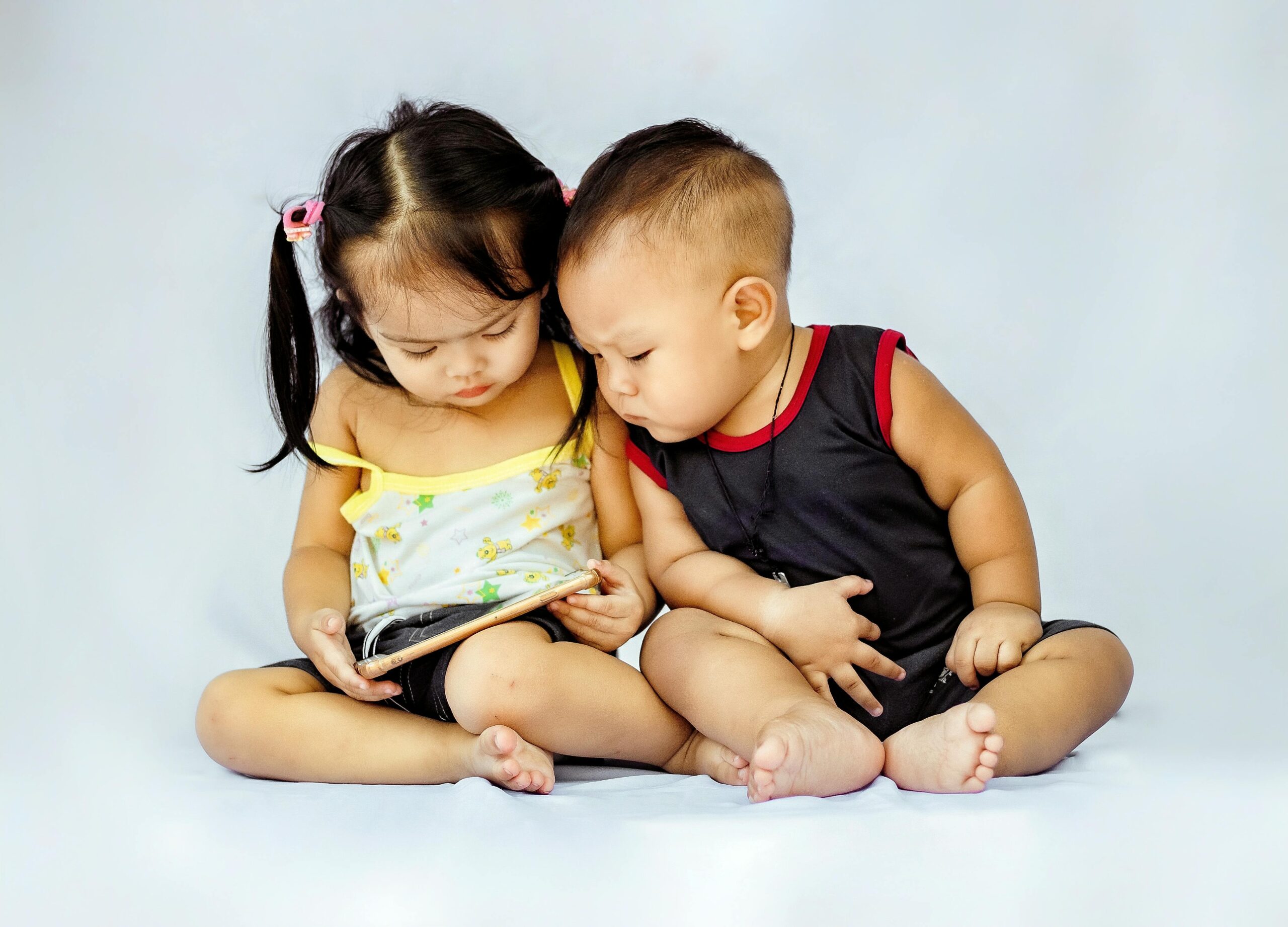 Two young children sitting together and exploring a tablet device in a studio setting.